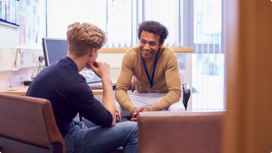 2 men in therapy session smiling and talking. 2 men in casual clothing in therapy setting.